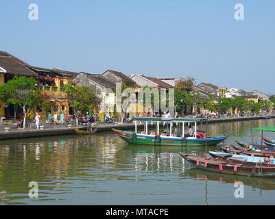 HOI AN, VIETNAM - 19. MÄRZ 2018: Schönen Tag in Hoi An Altstadt mit Blick auf die traditionellen Boote, gelbe Häuser am Ufer des Flusses, und die Touristen Stockfoto