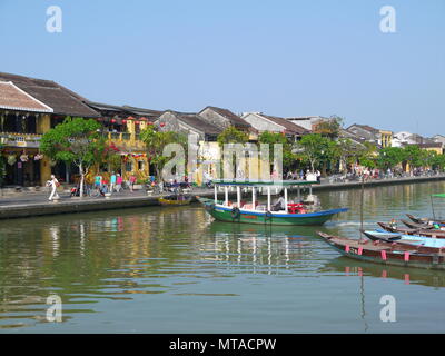 HOI AN, VIETNAM - 19. MÄRZ 2018: Schönen Tag in Hoi An Altstadt mit Blick auf die traditionellen Boote, gelbe Häuser am Ufer des Flusses, und die Touristen Stockfoto