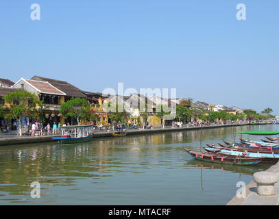 HOI AN, VIETNAM - 19. MÄRZ 2018: Schönen Tag in Hoi An Altstadt mit Blick auf die traditionellen Boote, gelbe Häuser am Ufer des Flusses, und die Touristen Stockfoto