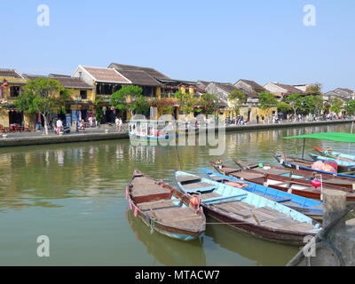 HOI AN, VIETNAM - 19. MÄRZ 2018: Schönen Tag in Hoi An Altstadt mit Blick auf die traditionellen Boote, gelbe Häuser am Ufer des Flusses, und die Touristen Stockfoto