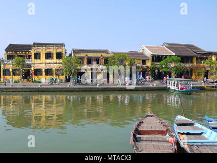 HOI AN, VIETNAM - 19. MÄRZ 2018: Schönen Tag in Hoi An Altstadt mit Blick auf die traditionellen Boote, gelbe Häuser am Ufer des Flusses, und die Touristen Stockfoto