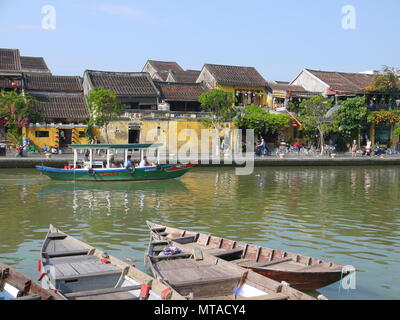 HOI AN, VIETNAM - 19. MÄRZ 2018: Schönen Tag in Hoi An Altstadt mit Blick auf die traditionellen Boote, gelbe Häuser am Ufer des Flusses, und die Touristen Stockfoto