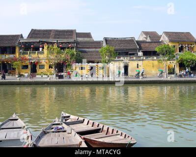 HOI AN, VIETNAM - 19. MÄRZ 2018: Schönen Tag in Hoi An Altstadt mit Blick auf die traditionellen Boote, gelbe Häuser am Ufer des Flusses, und die Touristen Stockfoto