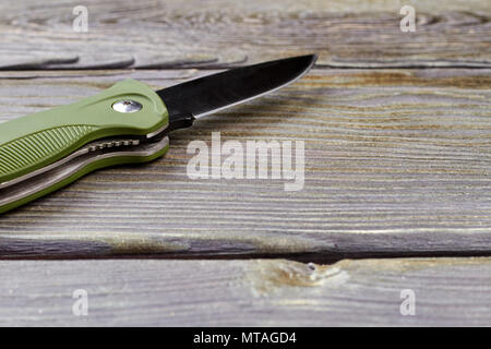 Verschluss - Messer auf Holz, aus der Nähe. Grüne Messer mit der scharfen Klinge auf Holz- Hintergrund. Stockfoto
