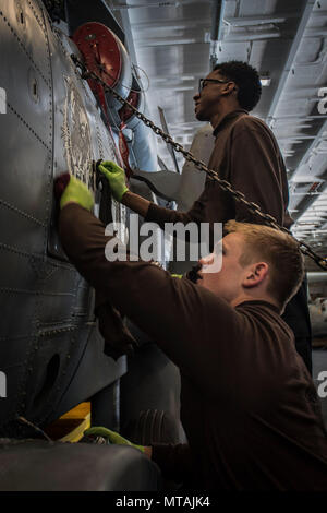 Pazifik (21. April 2017) - Flieger Sarek Schilde, Front, und Luftfahrt strukturellen Mechaniker Airman Lehrling Spencer Bedford sauber einem MH-60R Seahawk, zugeordnet zu den Battlecats der Hubschrauber Maritime Strike Squadron (HSM) 73, im Hangar Bay an Bord der Flugzeugträger USS Theodore Roosevelt (CVN 71). Theodore Roosevelt ist unterwegs durch eine maßgeschneiderte Schiff training Verfügbarkeit vor der Küste von Kalifornien. Stockfoto