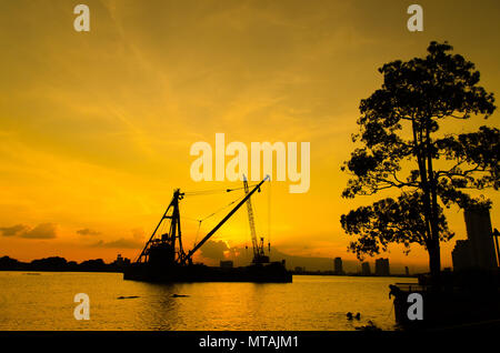 Silhouette Baustelle schweben über Fluss mit Reflexion auf den Sonnenuntergang. Bau Konzept. Stockfoto