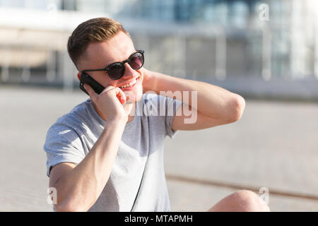 Skateboarder gekleidet in grauen T-Shirt und Sonnenbrille sprechen von Smartphone Stockfoto
