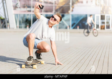 Skateboarder macht selfie auf Skateboard, low ride Position vor modernes Gebäude Stockfoto