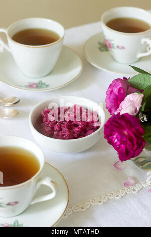 Stau in die Blütenblätter der Damaskus Rose, eine Tasse grünen Tee und eine Vase mit Rosen auf einem Leuchttisch. Rustikaler Stil, selektiven Fokus. Stockfoto