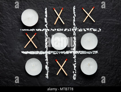 Tic Tac Toe xo Spiel mit Kerzen und Streichhölzer auf strukturierte schwarze Oberfläche. Konzept der tun oder sterben und Leben oder Tod. Von oben nach unten aus der Nähe ansehen. Stockfoto