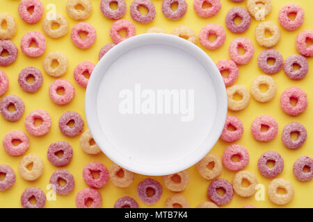 Ansicht von oben in eine Schüssel Milch auf bunten Müsli Ringe auf gelbem Hintergrund Stockfoto