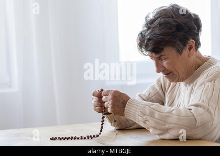 Traurig, Senior woman holding einen Rosenkranz und zu Hause beten Stockfoto