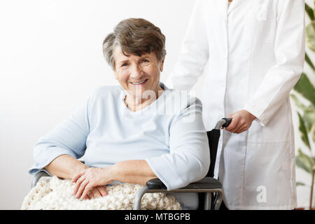 Betreuer und lächelnd behinderte ältere Frau im Rollstuhl Stockfoto