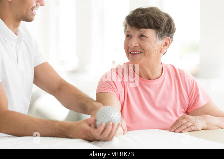 Patienten im Krankenhaus mit einem grau, gespickt Rehabilitation Kugel in der rechten Hand während der Physiotherapie Stockfoto