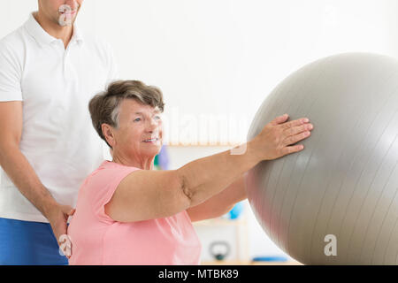 Ältere Patienten In einer isometrischen Physiotherapie Sitzung mit einem grauen Fit Ball und ein Physiotherapeut Stockfoto