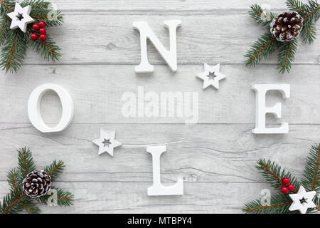 Noel mit weißen Buchstaben auf Holz Holz Hintergrund mit Tannenbaum Zweige, Holz- Sternen verziert geschrieben, verschneite Tannenzapfen und rote Beeren. Stockfoto