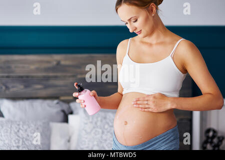 Junge schwangere Frauen, die Sahne auf den Bauch Stockfoto