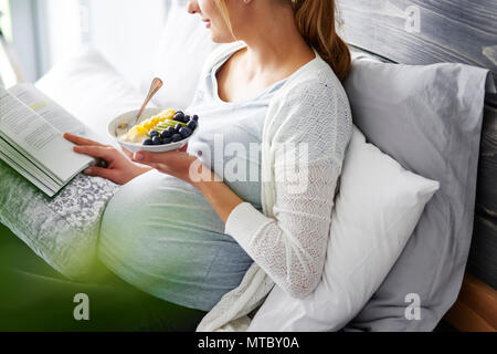 Junge Mutter essen und lesen Buch zu Hause Stockfoto