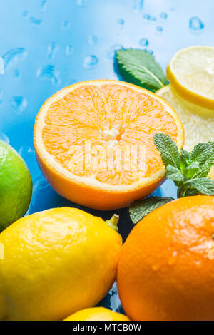 Vielzahl von Zitrusfrüchten Bio-früchten ganz und halbiert Orangen in Scheiben geschnittene Zitronen Limonen frische Minze auf blauem Hintergrund mit Wassertropfen. Morgen Sonnenlicht. Stockfoto