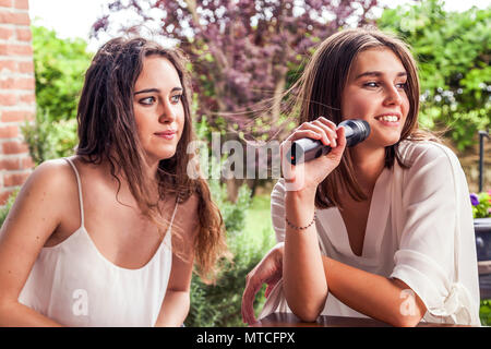 Zwei junge weibliche Freunde Spaß singen ein neues Lied am Mikrofon Stockfoto