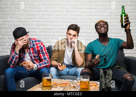 Drei attraktive, stattlich, emotionale Menschen Fernsehen, Sorge, Jubeln, Zeigefinger, Pizza, Bier, Alkohol im Wohnzimmer sitzen Stockfoto