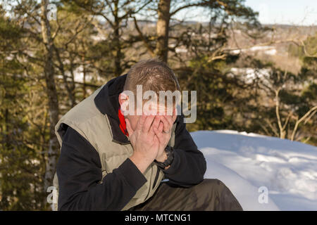 Mitte nach 40 s kaukasischen Mann sitzen draußen im Schnee im Winter mit Kopf in den Händen, die umgekippt Stockfoto