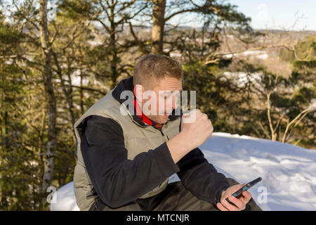 Mitte nach 40 s kaukasischen Mann sitzen draußen im Schnee im Winter, die gute Nachrichten auf seinem Smartphone Stockfoto