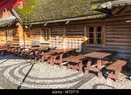 Wand von Rundholz. Dekoration aus Holz. Holzfenster. Das hölzerne Dach ist mit Holzschindeln gedeckt. Auf dem hölzernen Schindeln wächst Moos. Stockfoto