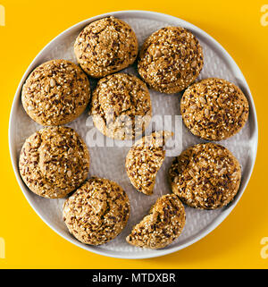 Frisch gebackene Oatmeal cookies sprengte mit Sonnenblumenkernen, Leinsamen und Sesam. Gesundes Gebäck in einer Platte auf gelbem Hintergrund Stockfoto