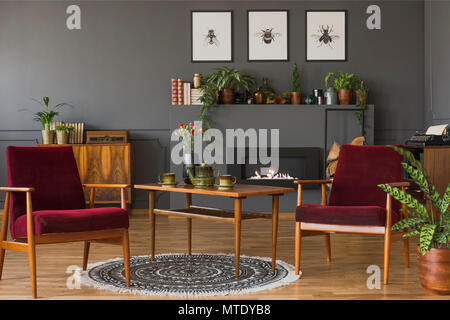 Dunkel rot Holz Sessel in Vintage flachbild Interieur mit Plakaten auf graue Wand über dem Kamin. Real Photo Stockfoto