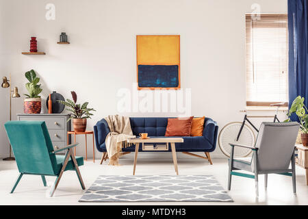 Real Photo eines navy blue Orange Sofa mit Kissen und ein Kunstwerk oben in den hellen und geräumigen Wohnzimmer Interieur mit zwei retro Sessel Stockfoto