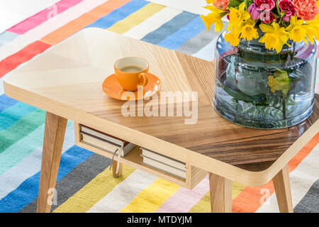 Nahaufnahme eines hölzernen Tisch mit einer Tasse Kaffee und einen Strauß Blumen auf den bunt gestreiften Teppich Stockfoto