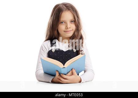 Kleines Mädchen mit einem Buch an einem Tisch sitzen, und wenn man die Kamera auf weißem Hintergrund Stockfoto