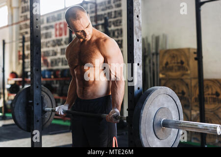 Seitenansicht der männlichen Athleten an seine Muskeln suchen und heben Barbell in der Turnhalle Stockfoto