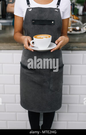 Nicht erkennbare Frau mit Schürze, im Cafe stehend mit Tasse Kaffee Stockfoto