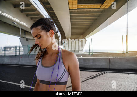 Junge sportliche Frau, die unter einer Brücke mit Seil springen am Hals Stockfoto