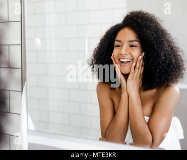 Glückliche Frau, die Ihre Haut bewundern vor dem Badezimmerspiegel, Gesicht mit den Händen berühren. Stockfoto