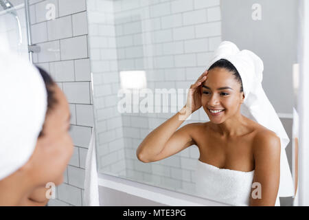 Schöne junge Frau berühren ihre Haut während im Badezimmerspiegel suchen Stockfoto