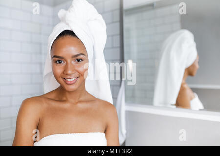 Nahaufnahme, Porträt einer schönen Frau in Handtücher rund um Kopf und Körper gewickelt, stehend im Bad Stockfoto