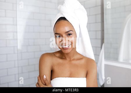 Portrait einer attraktiven jungen Frau in ihrem Bad zu Hause, wickelte ein Handtuch um den Kopf Stockfoto