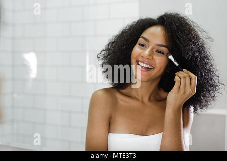 Schöne junge Frau mit Bürste in einen Spiegel schauen und Anwendung von Make-up Stockfoto