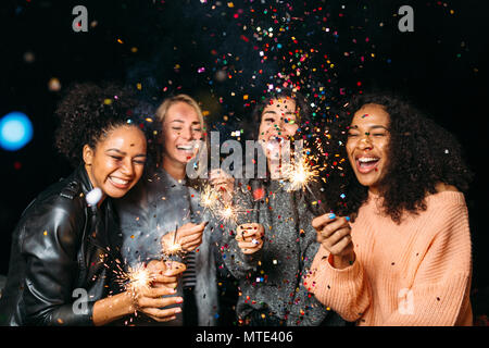 Gerne Freunde. Gruppe von lächelnden Frauen holding Wunderkerzen unter Konfetti Stockfoto