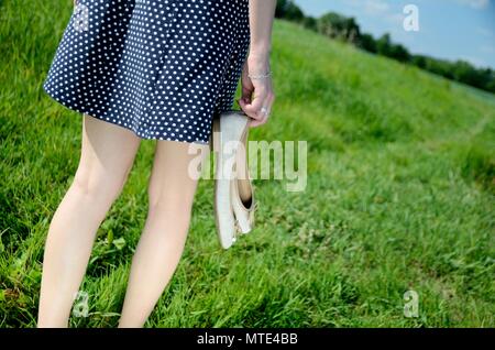 Weibliche Wege auf dem Gras mit barfuß. Junge Frau genießt Spaziergang im Freien, Natur, grüne Wiesen und blauer Himmel. Stockfoto