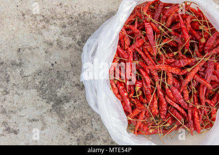 Getrocknete Chilis aus weißem Kunststoff Beutel auf Betonboden platziert Stockfoto