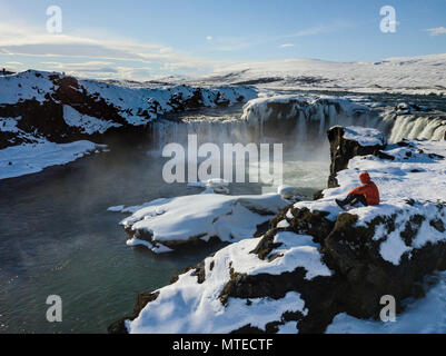 Luftaufnahme, Mann, der vor Wasserfall Góðafoss, Godafoss im Winter mit Schnee und Eis, Norðurland djupivogur Stockfoto