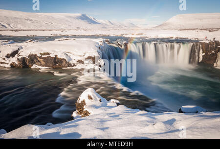 Regenbogen am Wasserfall Góðafoss, Godafoss im Winter mit Schnee und Eis, Wasser des Flusses Skjálfandafljót Stockfoto