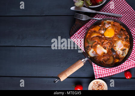Shakshuka mit Fladenbrot in der Pfanne. Im Nahen und Mittleren Osten traditionelles Gericht. Spiegeleier mit Tomaten, Paprika, Gemüse und Kräuter. Flach. Ansicht von oben. Stockfoto
