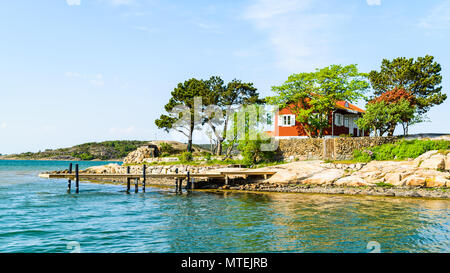 Wunderschöne Insel mit einem roten Haus und ein Pier. Einige Bäume wachsen auf der kleinen Insel und der umliegenden Landschaft ist sonnig und ruhig. Stockfoto