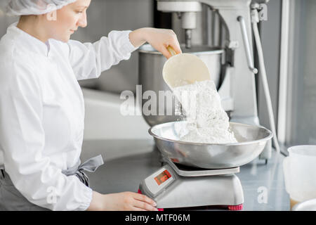 Frau Konditor in Uniform wiegen Zutaten für Gebäck in der Bäckerei verarbeitenden Gewerbe Stockfoto