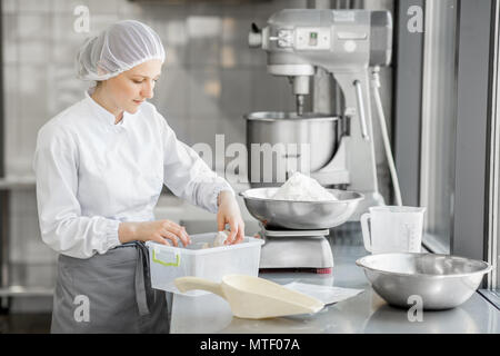 Frau Konditor in Uniform wiegen Zutaten für Gebäck in der Bäckerei verarbeitenden Gewerbe Stockfoto